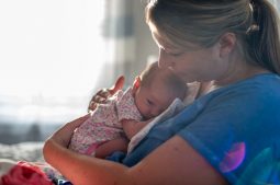 Young woman sitting on bed holding newborn daughter